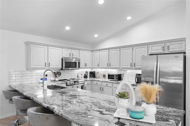 kitchen with sink, appliances with stainless steel finishes, lofted ceiling, tasteful backsplash, and white cabinets