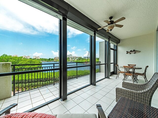 sunroom with ceiling fan and a water view