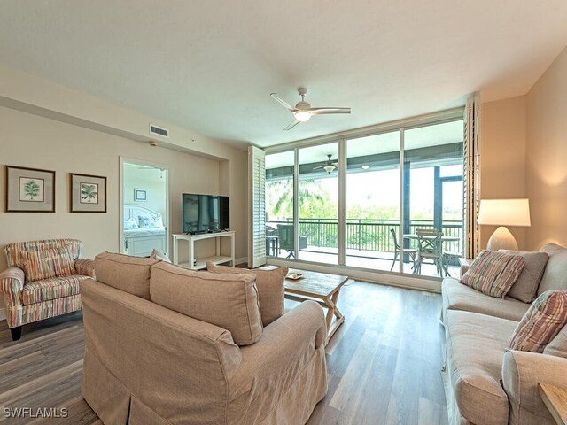 living room with ceiling fan, wood-type flooring, and a wall of windows