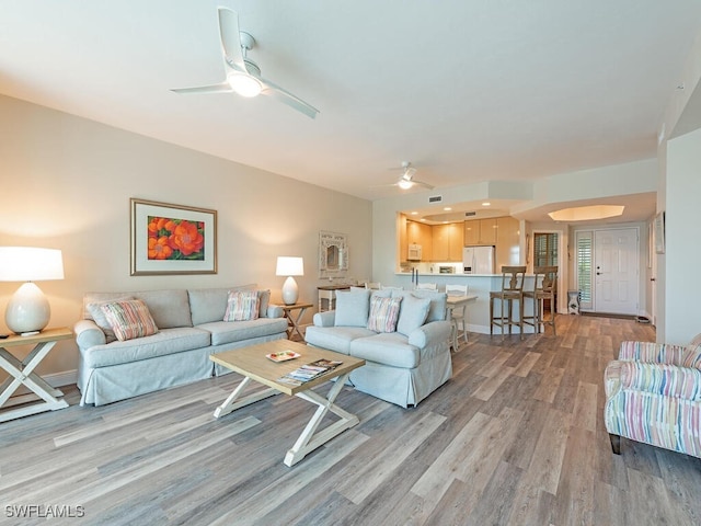 living room featuring ceiling fan, visible vents, light wood-style flooring, and baseboards