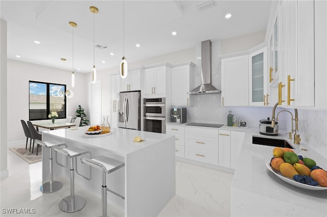 kitchen with white cabinetry, hanging light fixtures, stainless steel appliances, a center island, and wall chimney exhaust hood