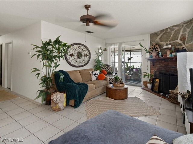 tiled living room featuring ceiling fan, a textured ceiling, and a large fireplace