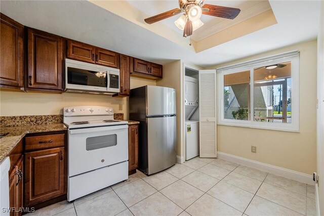 kitchen featuring baseboards, ornamental molding, a tray ceiling, stainless steel appliances, and stacked washing maching and dryer