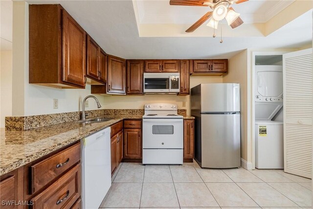 kitchen featuring appliances with stainless steel finishes, a raised ceiling, light stone countertops, stacked washer and dryer, and sink