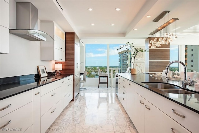 kitchen featuring white cabinetry, hanging light fixtures, wall chimney exhaust hood, and sink