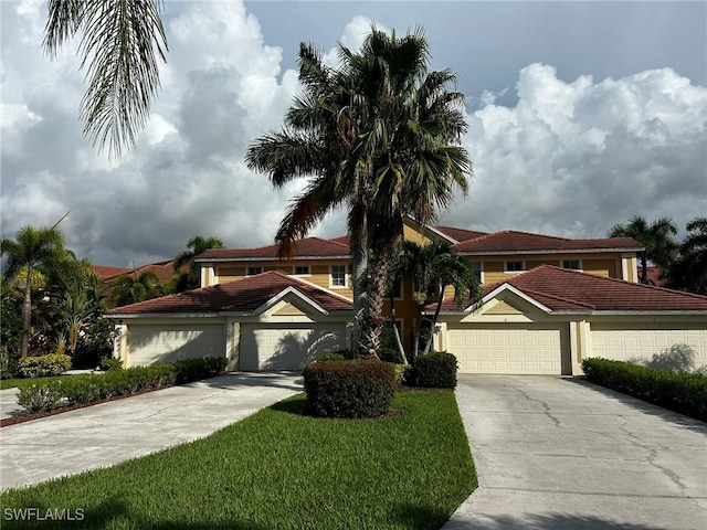 mediterranean / spanish-style house with a garage, concrete driveway, a tiled roof, stucco siding, and a front yard