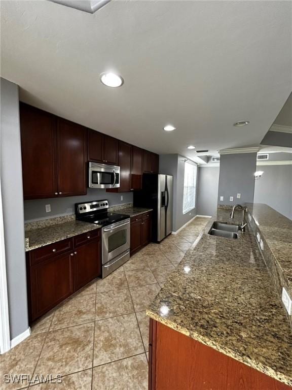 kitchen with stone counters, light tile patterned flooring, stainless steel appliances, a peninsula, and a sink