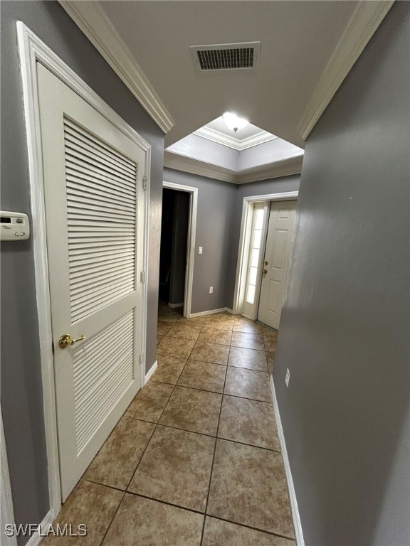 doorway featuring crown molding, light tile patterned floors, and a raised ceiling