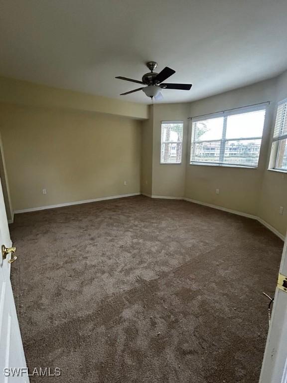 unfurnished room with ceiling fan, dark carpet, and baseboards