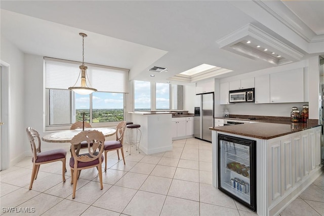 kitchen featuring kitchen peninsula, appliances with stainless steel finishes, a raised ceiling, pendant lighting, and white cabinets