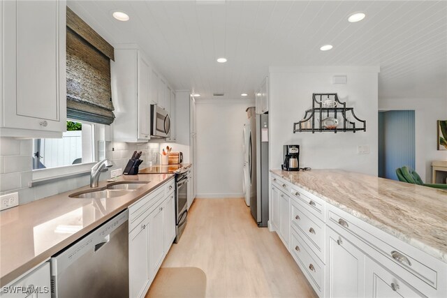 kitchen with white cabinetry, stainless steel appliances, light stone countertops, light hardwood / wood-style flooring, and sink