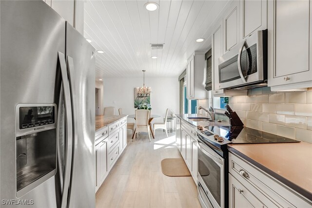 kitchen featuring white cabinets, appliances with stainless steel finishes, decorative light fixtures, light hardwood / wood-style floors, and sink