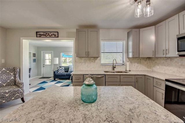 kitchen with gray cabinetry, stainless steel appliances, a sink, light stone countertops, and tasteful backsplash