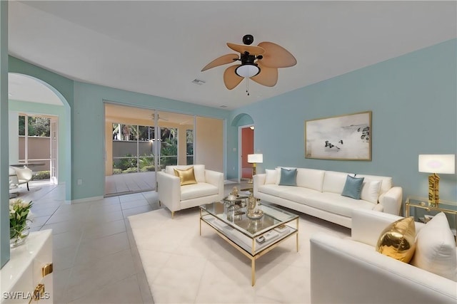 living area featuring arched walkways, light tile patterned floors, visible vents, ceiling fan, and baseboards