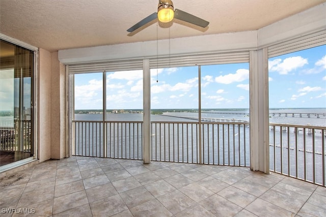 unfurnished sunroom featuring ceiling fan, a wealth of natural light, and a water view