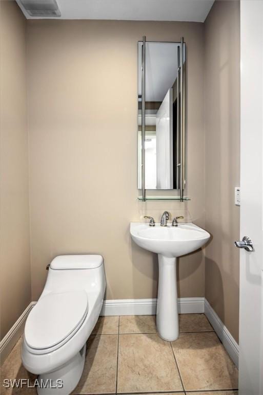 half bathroom featuring toilet, tile patterned floors, baseboards, and a sink