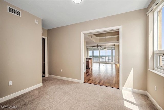 carpeted empty room with a notable chandelier and a tray ceiling