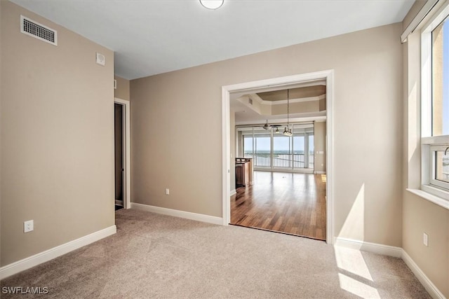 carpeted spare room with a notable chandelier, visible vents, baseboards, and a raised ceiling