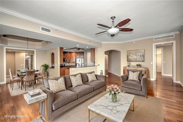 living area featuring arched walkways, ceiling fan, crown molding, and visible vents