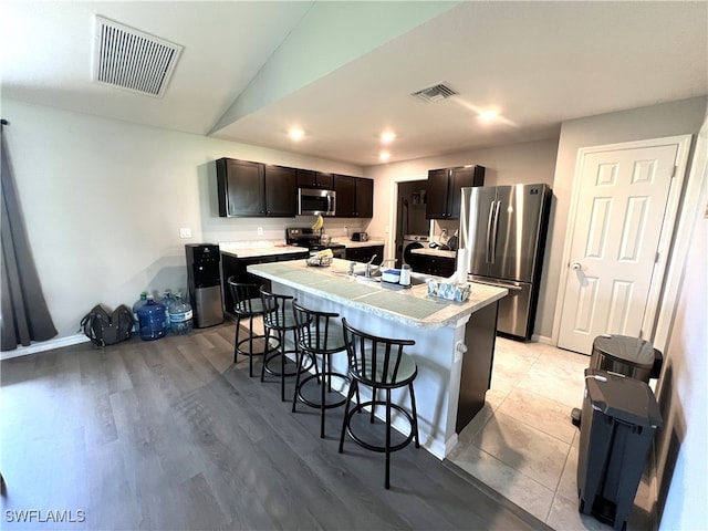 kitchen with appliances with stainless steel finishes, a kitchen bar, dark brown cabinetry, light wood-type flooring, and a center island