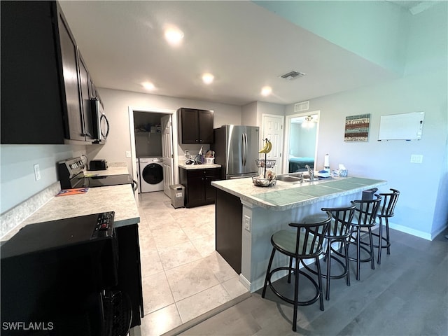 kitchen with appliances with stainless steel finishes, a kitchen bar, sink, a center island with sink, and washer / clothes dryer