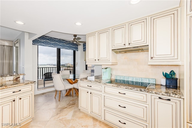 kitchen featuring ceiling fan, cooktop, cream cabinets, light stone countertops, and light tile patterned flooring