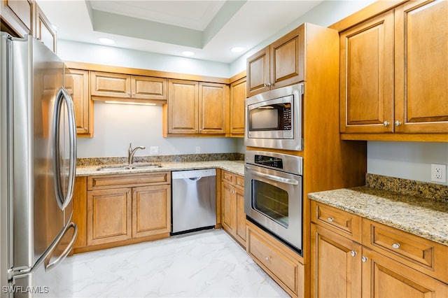 kitchen with sink, light stone counters, a tray ceiling, light tile patterned floors, and stainless steel appliances