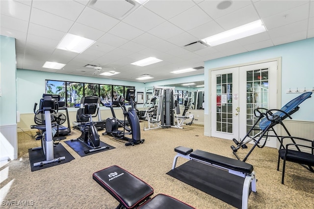 workout area featuring a paneled ceiling, ceiling fan, french doors, and wood walls