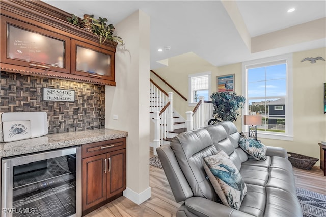 bar with wine cooler, decorative backsplash, light stone counters, and light wood-type flooring