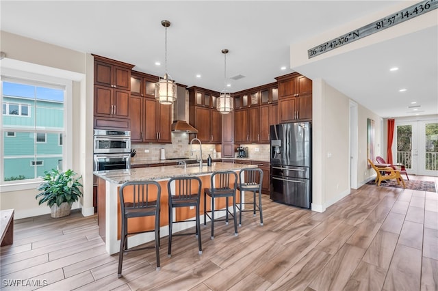 kitchen featuring pendant lighting, backsplash, a kitchen island with sink, light stone counters, and stainless steel appliances