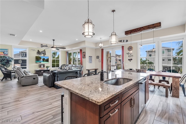 kitchen with a center island with sink, sink, hanging light fixtures, ceiling fan, and light stone countertops