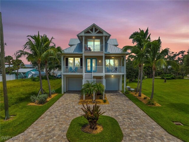 coastal home featuring a garage, covered porch, a yard, and french doors