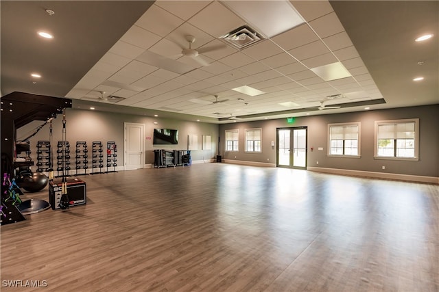 exercise room with a paneled ceiling, ceiling fan, hardwood / wood-style flooring, and french doors