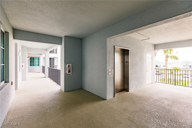 corridor featuring light colored carpet, elevator, and a textured ceiling