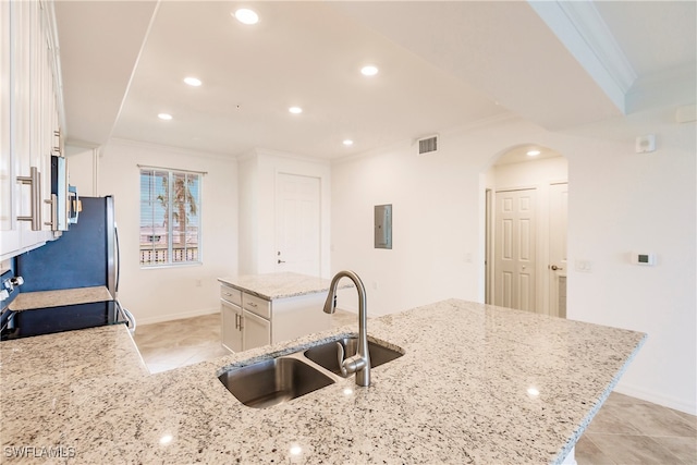 kitchen with sink, light stone counters, light tile patterned floors, stove, and white cabinets