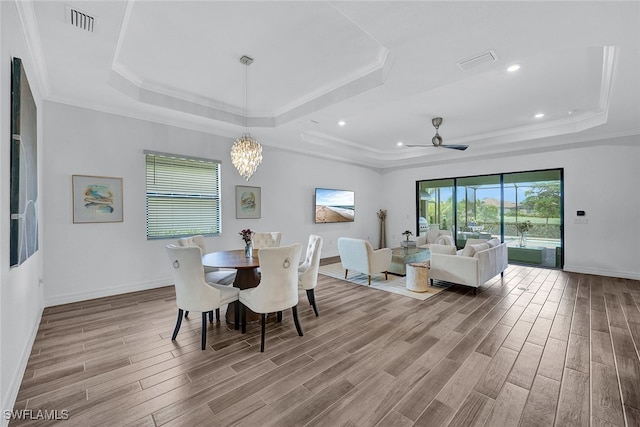 dining space featuring ceiling fan with notable chandelier, crown molding, a tray ceiling, and wood-type flooring