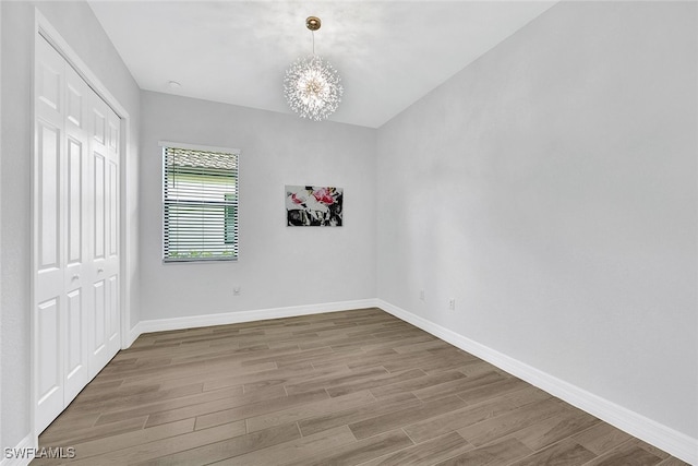 empty room with wood-type flooring and an inviting chandelier