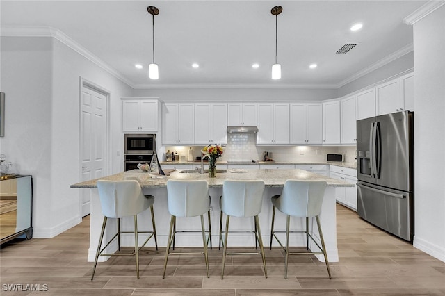 kitchen featuring light hardwood / wood-style floors, appliances with stainless steel finishes, pendant lighting, and an island with sink