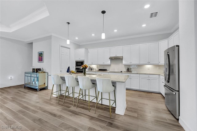 kitchen featuring stainless steel refrigerator, built in microwave, white cabinetry, hanging light fixtures, and a kitchen island with sink