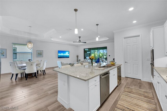 kitchen with a raised ceiling, a kitchen island with sink, light hardwood / wood-style floors, decorative light fixtures, and stainless steel appliances