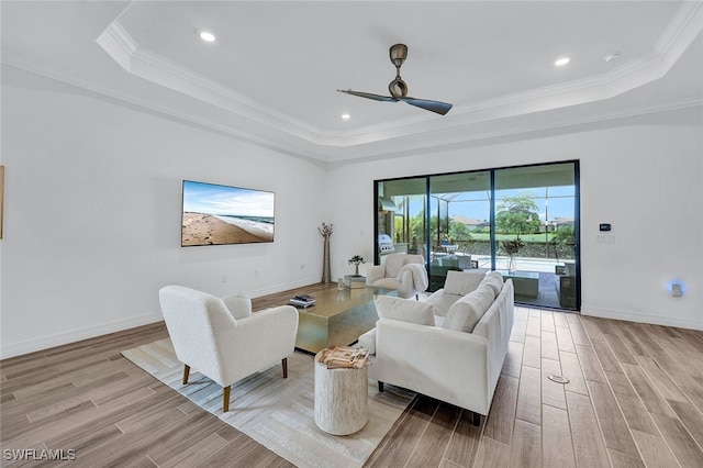 living room featuring ceiling fan, ornamental molding, a tray ceiling, and light hardwood / wood-style flooring