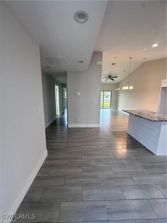 empty room featuring ceiling fan with notable chandelier, wood finish floors, vaulted ceiling, and baseboards