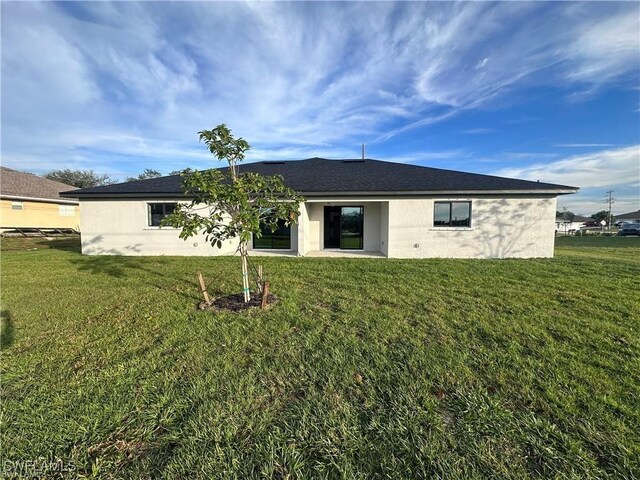 rear view of property featuring a lawn and stucco siding