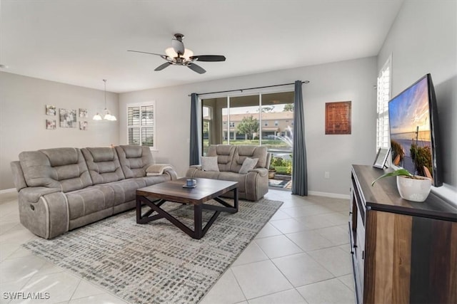 living room with light tile patterned floors, ceiling fan with notable chandelier, and baseboards