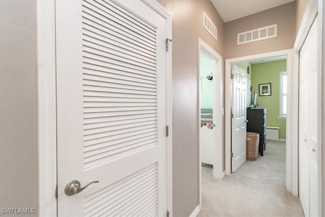 hallway with light colored carpet, visible vents, and baseboards