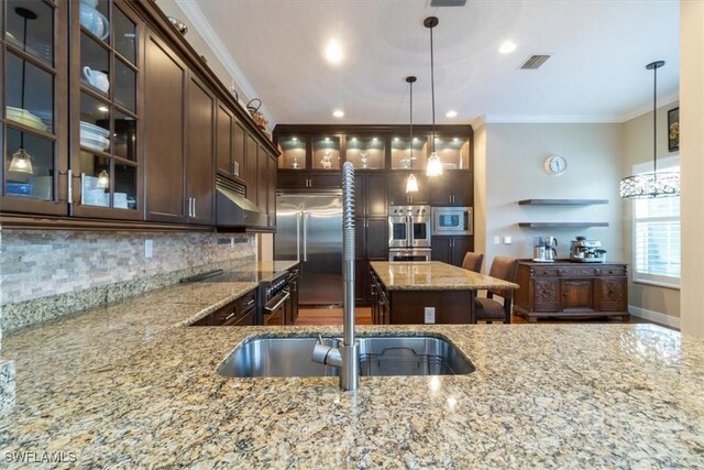 kitchen featuring pendant lighting, built in appliances, light stone countertops, and crown molding