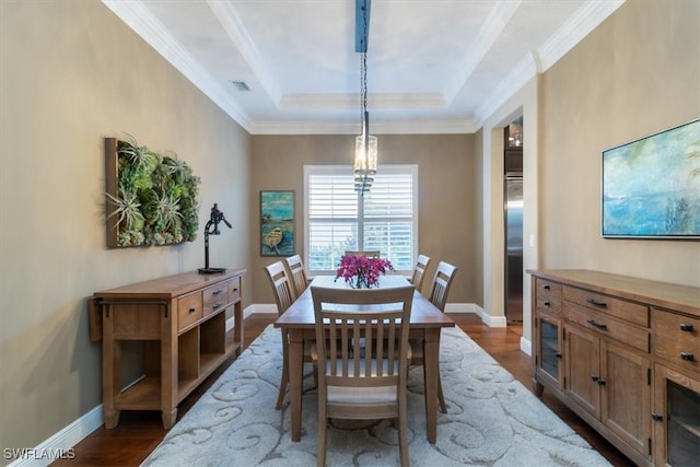 dining room with a raised ceiling, wood-type flooring, and crown molding