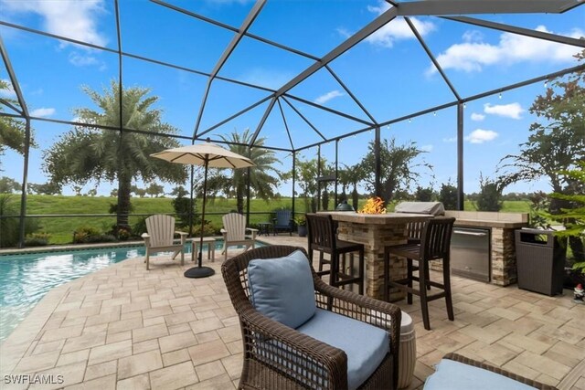 view of patio / terrace featuring a bar, an outdoor kitchen, and a lanai