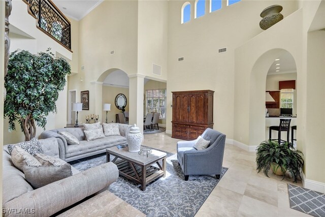 living room featuring decorative columns, crown molding, and a high ceiling