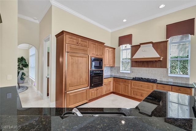 kitchen featuring backsplash, black appliances, crown molding, dark stone countertops, and custom range hood